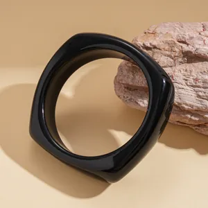Detailed macro view of a high-gloss black geometric chunky bangle on a stone prop.