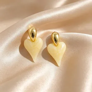 Detailed macro view of heart-shaped cream resin earrings with 18K gold plating on silk