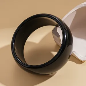 Detailed view of a minimalist glossy black round bangle showcasing its smooth surface