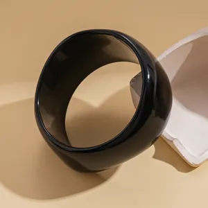 Close-up of a wide glossy black circular bangle on a minimalist beige background
