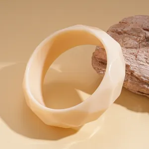 Close-up of a cream-colored faceted geometric resin bangle on a warm-toned surface