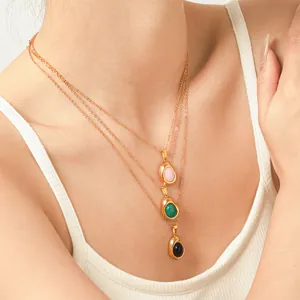 Close-up of gold-plated bean pendants with pink, green, and black stones on necklaces