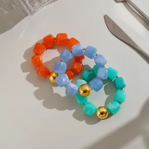 Nahaufnahme von drei bunten quadratischen Harzperlen-Armbändern mit einer großen Goldperle