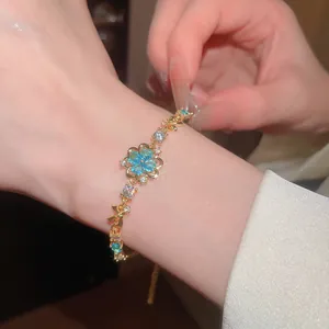 Close-up of sea blue zircon flower bracelet on wrist with elegant gold chain.
