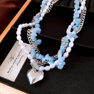 Détail d'un collier multicouche avec perles blanches, pierres bleues et cœur argenté.