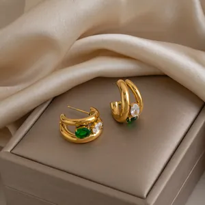 Gros plan sur des boucles d'oreilles en C dorées 18K avec zircons verts et blancs