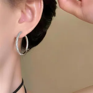 Close-up detail of asymmetrical silver hoop earrings with pave-set shimmering stones