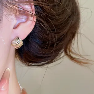 Gros plan d'une boucle d'oreille carrée géométrique dorée avec texture martelée sur l'oreille.