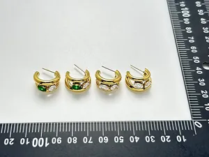 Vue détaillée de créoles dorées en forme de C avec zircons et règle de mesure graduée.