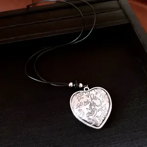 Detailed macro view of silver heart pendant with elegant floral engravings on black cord