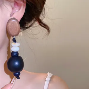 Detailaufnahme eines einzigartigen Tropfenohrrings aus Holz und schwarzem Acryl am Ohr