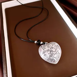 Macro view of vintage silver heart pendant with intricate floral engravings on black cord.