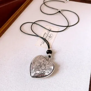 Detail shot of a silver heart pendant necklace with floral engraving and black cord.
