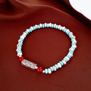 Close-up of ethnic beaded bracelet featuring turquoise beads and engraved silver tube.