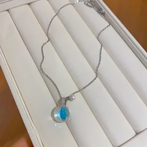 Gros plan d'un collier argenté avec pendentif boule en résine transparente et un centre bleu