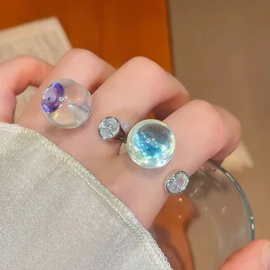 Gros plan d'une bague en résine transparente avec sphère irisée et zircons sur main.