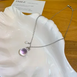 Gros plan d'un collier avec pendentif sphère en résine violette sur plateau