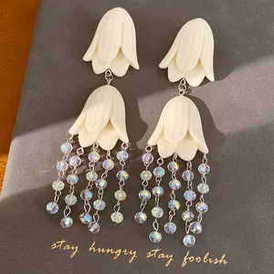 Detailed view of elegant cream acrylic flower tassel earrings with iridescent beads on a gray background
