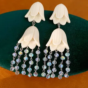Close-up of elegant flower tassel earrings with iridescent beads on a green stand