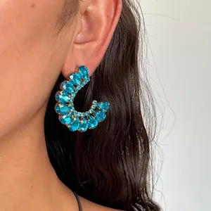 Detailopname van luxe sprankelende blauwe strass C-vormige oorbellen op een modeloor.