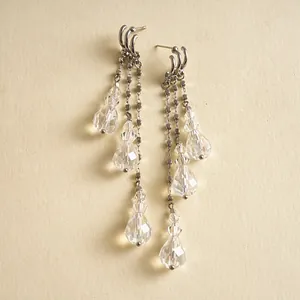 Détail rapproché de boucles d'oreilles à pompons argentés avec gouttes en verre clair