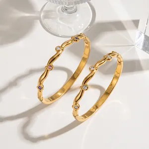Primo piano di bracciali ondulati in acciaio dorato con pietre di zircone colorate