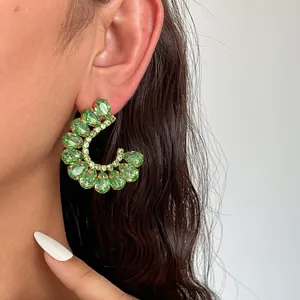 Detailopname van luxe C-vormige oorbellen met sprankelende groene druppelkristallen.