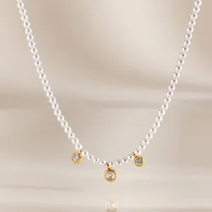 Primo piano di una collana di perle acriliche con tre ciondoli in zircone dorati