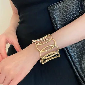 Detailansicht eines goldenen ovalen offenen Armreifs getragen mit schwarzem Kleid und Tasche