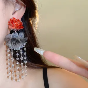 Detail view of resin flower tassel earrings with red and grey blossoms worn by model