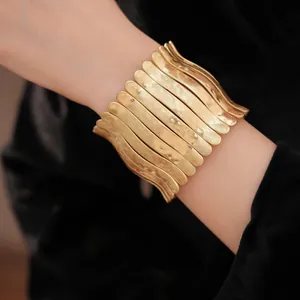 Vue détaillée d'un bracelet manchette plissé en métal doré sur un poignet élégant
