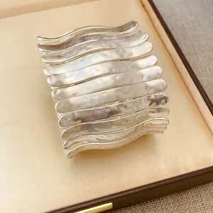 Gros plan d'un bracelet manchette métallique à texture ondulée dans un coffret à bijoux
