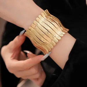Gros plan d'un large bracelet manchette extensible en métal doré martelé au poignet.