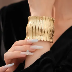 Gros plan d'un large bracelet manchette en métal doré plissé avec détails de texture martelée