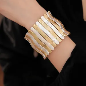 Gros plan d'un large bracelet métallique plissé aux finitions dorées et argentées