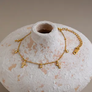 Gedetailleerd overzicht van gouden kruisarmband met zirkoonhangers op getextureerde vaas