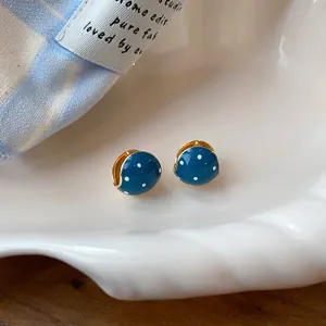 Close-up of retro blue enamel huggie earrings with white polka dots on a white dish.