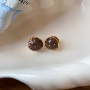 Detailed macro view of Maillard brown polka dot enamel earrings on a creamy seashell