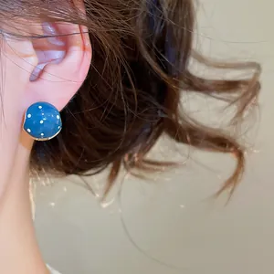 Close-up view of a vintage blue polka dot enamel earring worn on a model's ear