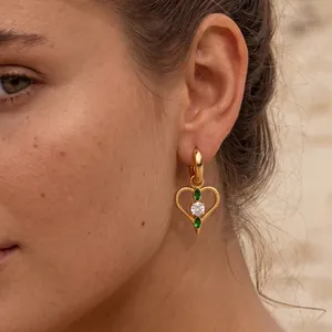 Nahaufnahme eines goldenen Herzohrrings mit grünen und weißen Zirkonia am Modell
