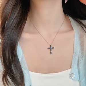 Primer plano de un collar con cruz de circón azul usado por una modelo sobre un escote blanco