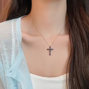 Primer plano de un elegante collar de cruz bañada en oro de 18k con circonitas azules