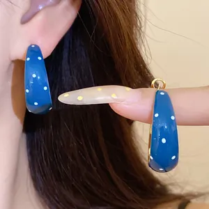 Detailed view of blue polka dot enamel hoop earrings worn on ear and held on finger