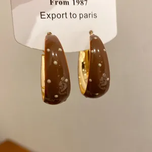 Close-up macro detail of brown enamel hoop earrings with white polka dot pattern