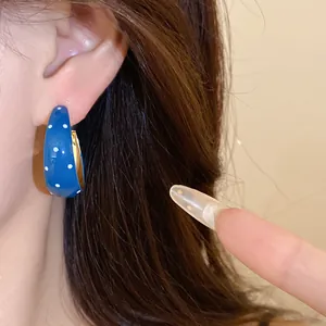 Detailed close-up view of blue drip oil hoop earring with white polka dots on ear