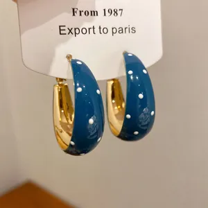 Close-up of blue enamel hoop earrings with white polka dots on a display card