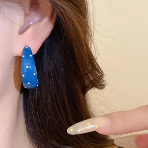 Macro detail of a vintage blue enamel earring with white polka dots worn on an ear lobe.
