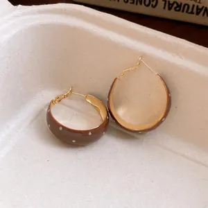 Detailed close-up of retro brown enamel hoop earrings featuring elegant white polka dots.