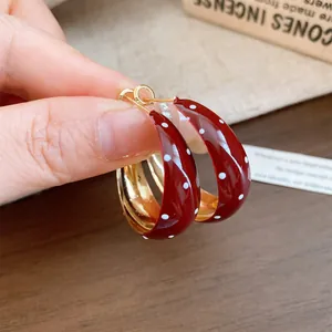 Close-up detail of retro red enamel hoop earrings with white polka dots and gold interior.