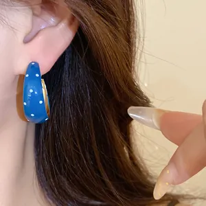 Macro view of blue enamel polka dot hoop earring worn on ear with dark hair background.